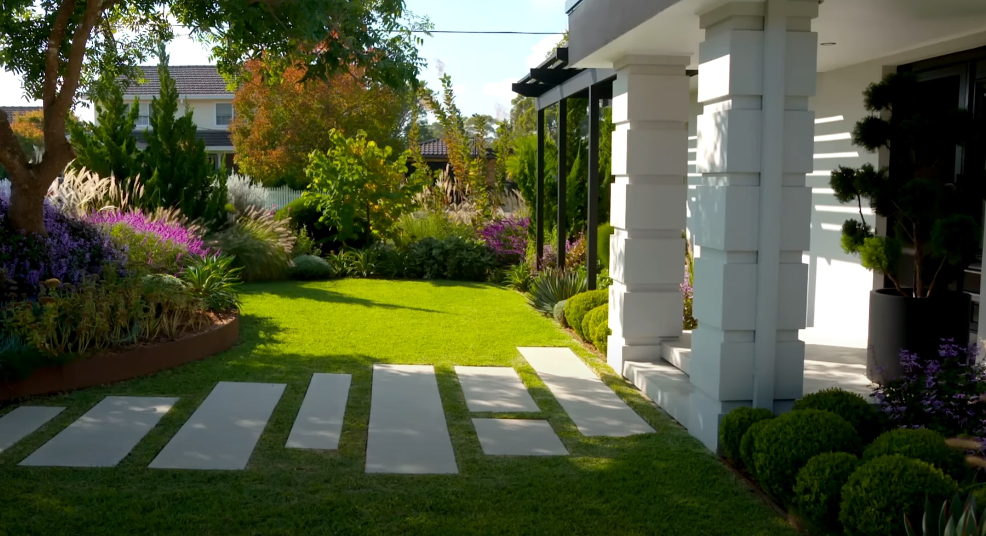 Front Yard Landscaping with Concrete Pavers and Colorful Plant Design Modern home entrance with concrete paver walkway, purple flowering plants, and professional landscape lighting