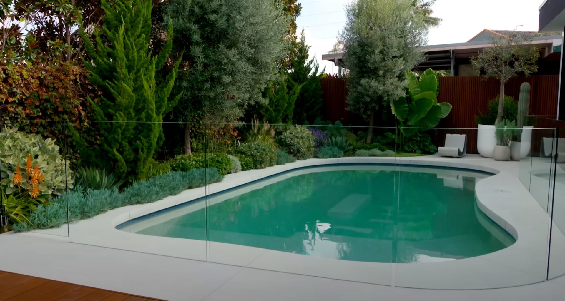 Pool Area Landscaping with Tropical Plants and Modern Design Modern pool area landscaping with lush tropical plants, glass safety fencing, and contemporary outdoor design