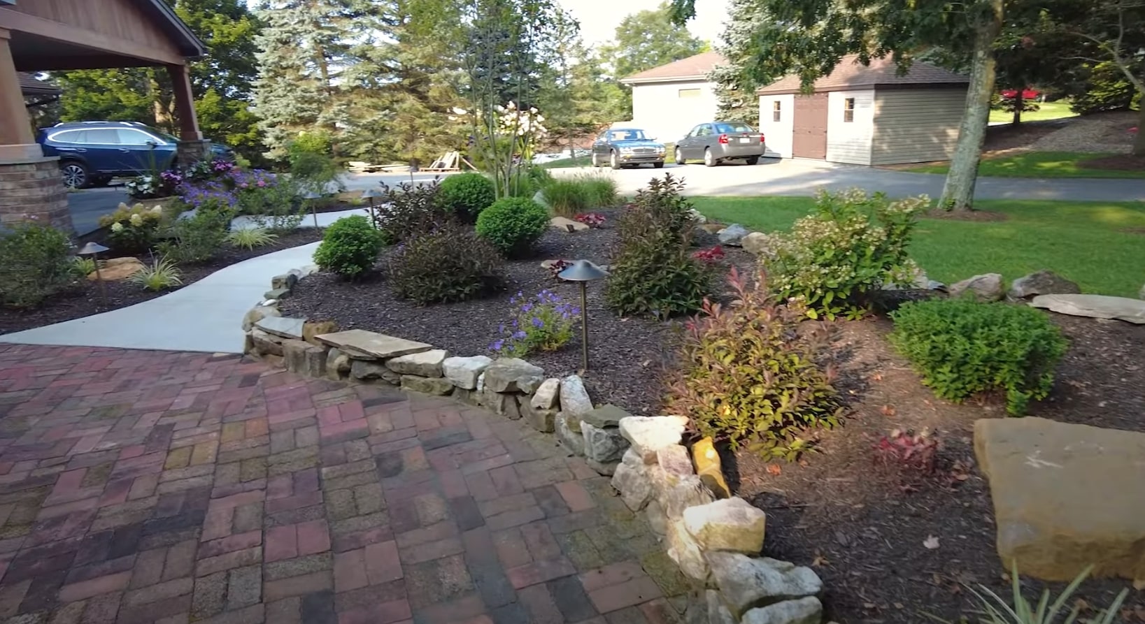 Residential Landscape Design with Stone Retaining Walls and Flower Gardens Professional landscaping design featuring curved stone retaining walls, colorful flower beds, and brick paver walkways